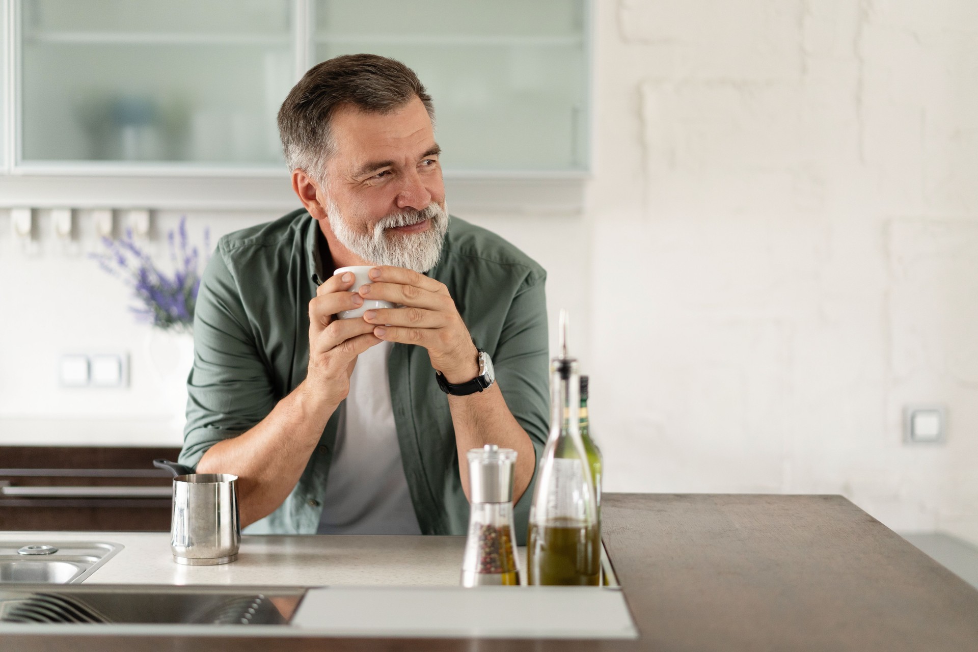 Happy mature man drinking coffee at home in the kitchen, enjoying hot drink in the morning on weekend.