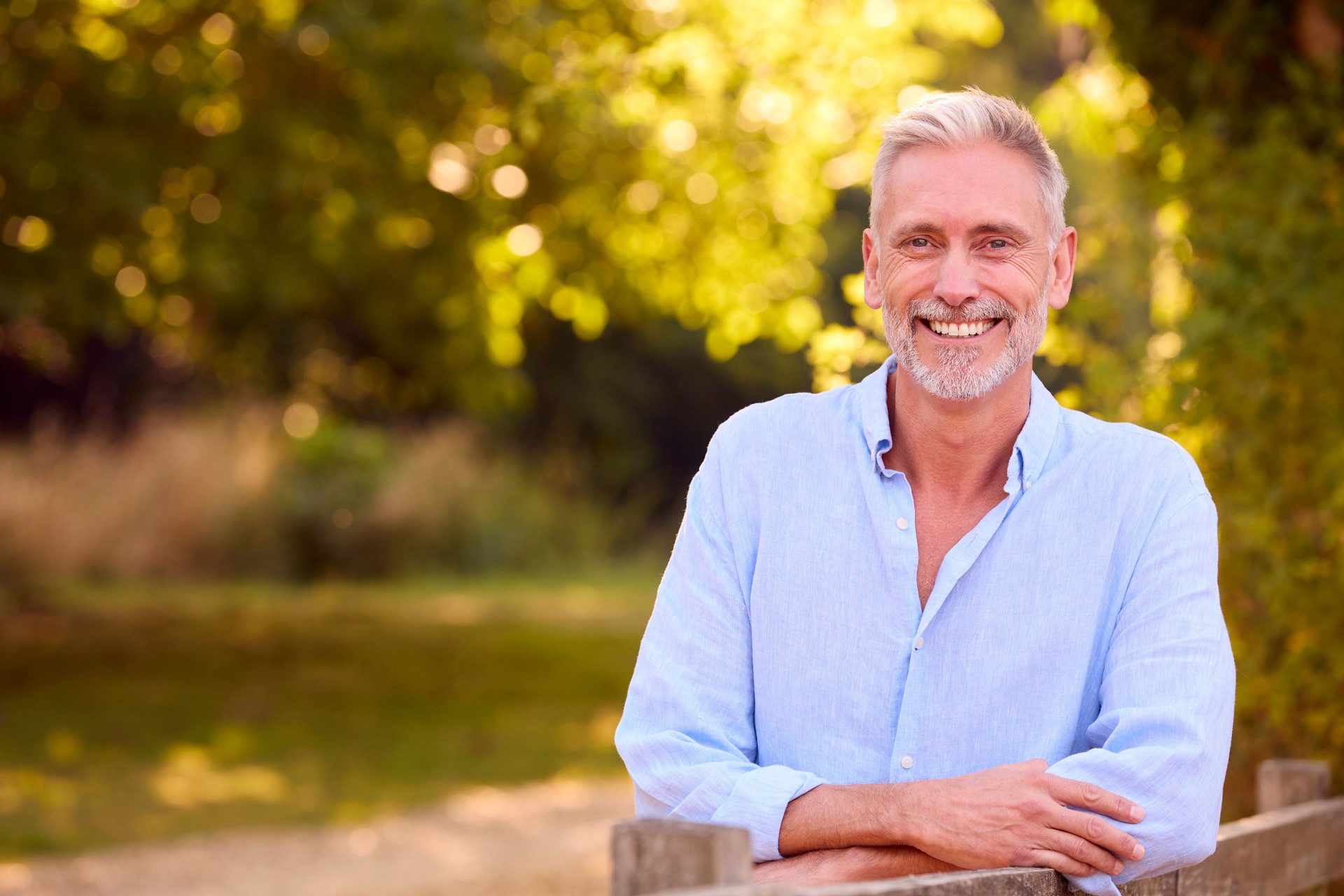 Portrait Of Casually Dressed Mature Man Leaning On Fence On Walk In Countryside